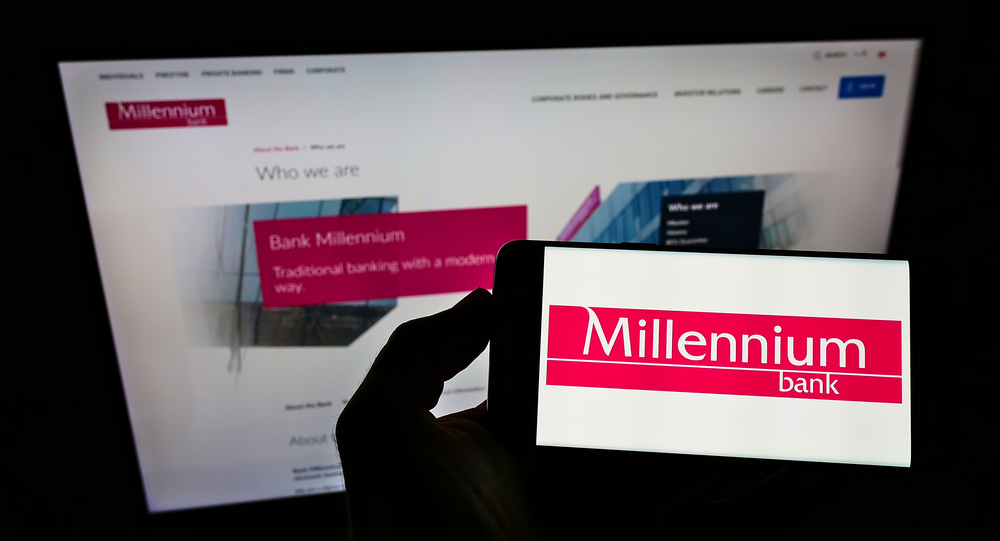 Osoba posiadająca smartfon z logo polskiej firmy finansowej Bank Millennium SA na ekranie przed stroną internetową.