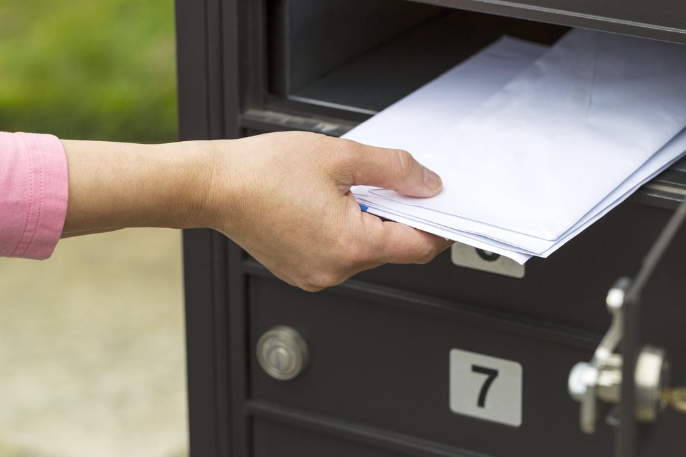 Ręka kobiety odbiera ze skrzynki pocztowej doręczoną korespondencję